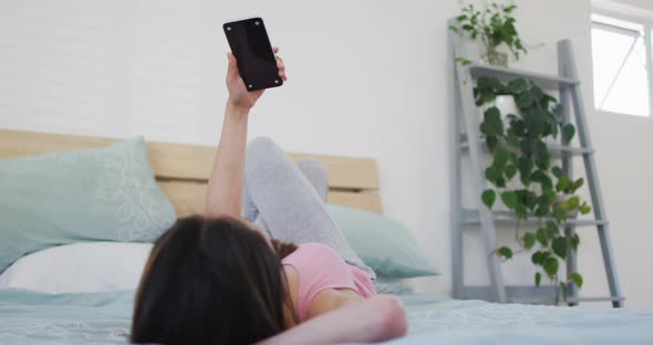 Asian woman lying on bed, using smartphone with copy space in the morning