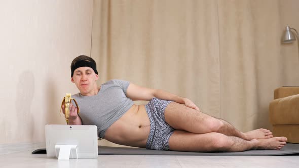 Feminine Man Eating Banana and Looking at Tablet While Lying on the Floor