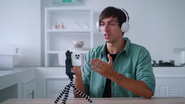 Young Man in Wireless Headphones is Talking on a Video Call Using His Mobile Phone