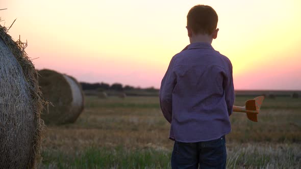 The Red-haired Boy Plays with a Toy Airplane on a Wheat Field with Bales