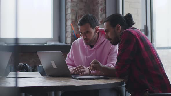 A Young Businessman with a Laptop Talks to a Colleague in the Office