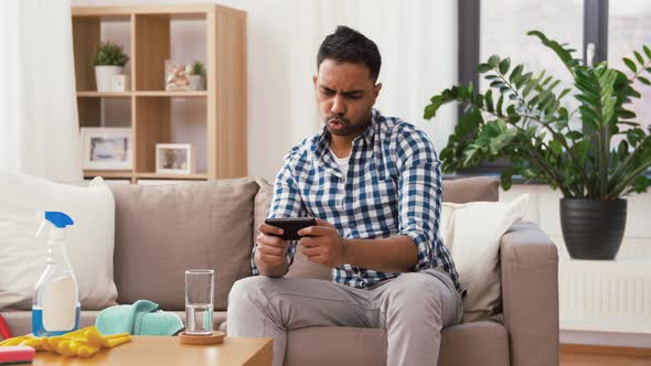 Man Playing Game on Smartphone After Cleaning Home 