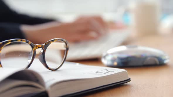 Close-up of personal organizer and spectacle while businesswoman working over computer