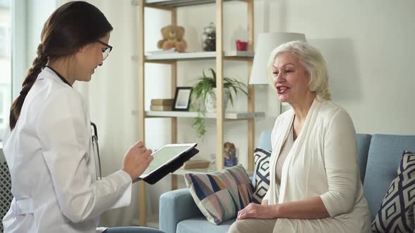 Young Nurse Using Tablet and Visiting Healthy Retirement Woman