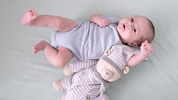 Newborn Baby Boy 3 Months Old Lies in Crib Nursery with Blue Clothes on His Back with Teddy Bear