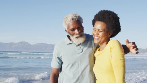 Happy african american couple walking and embracing on sunny beach