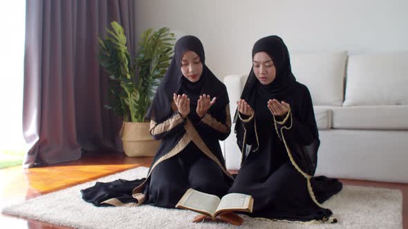 Young Muslim woman and female friend reading Quran and praying