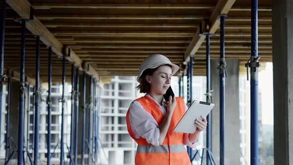 Engineer in safety jacket and helmet is talking on mobile phone on development construction site