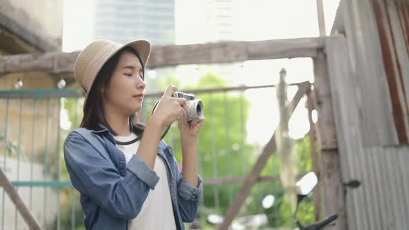 Beautiful young lady traveler wearing fedora hat taking a photo with a film camera at a small street