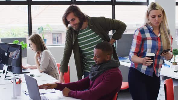 Diverse business people standing talking using a laptop in modern office