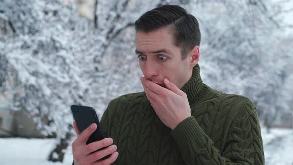 Shocked Man Reacting Message on Smartphone Covers His Mouth in Fright While Standing Winter Snowy