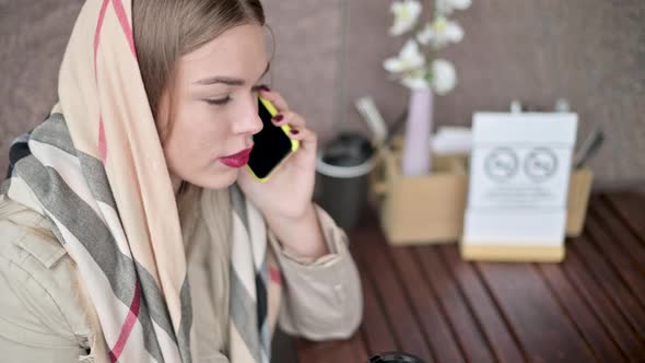 young woman in a cafe drinking coffee on the street and talking on the phone