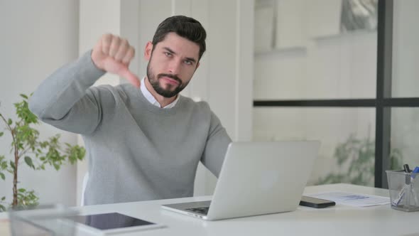 Young Man Showing Thumbs Down Sign While Using Laptop at Work