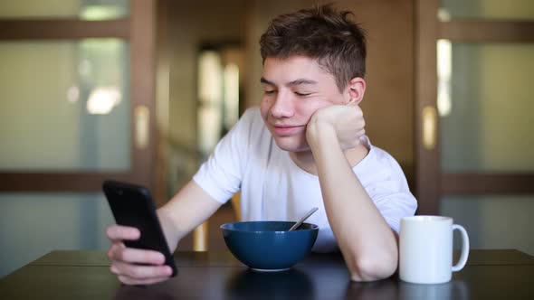 Teenager is texting on a smartphone over a plate of porridge during breakfast