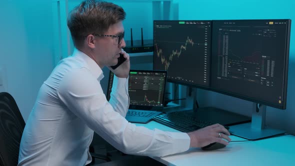 Financial trader working in office filled with computers conducting speaks on the phone