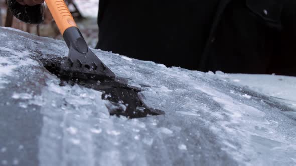 Person Hand Holds Ice Scraper and Cleans Vehicle Windshield