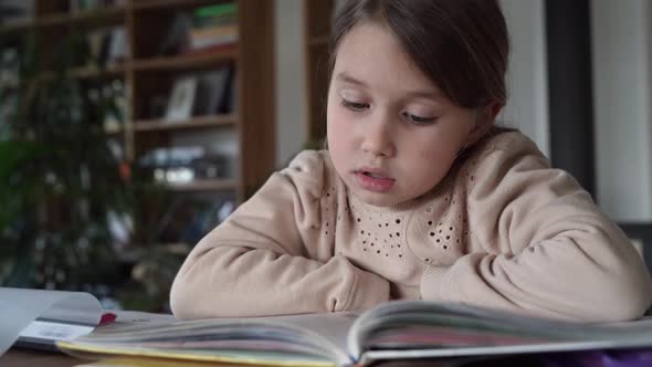 Little girl reading in exercise book sitting at home