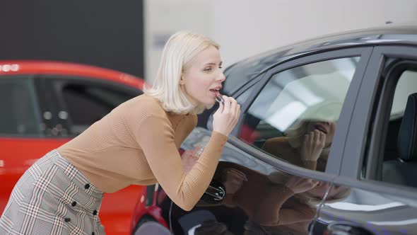 Side View of Confident Caucasian Blond Woman Applying Lipstick Using Side Window As Mirror in Car