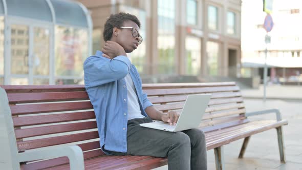 Young African Man with Neck Pain Using Laptop While Sitting Outdoor on Bench