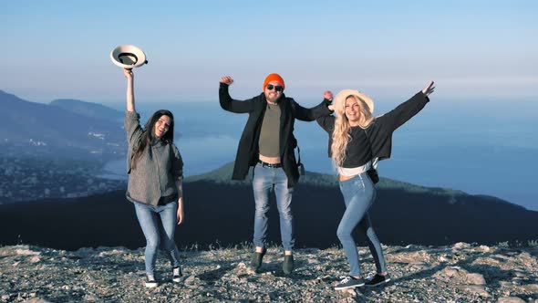 Group of Active Young Travelers Having Good Time Outdoor Smiling Jumping on Top of Mountain