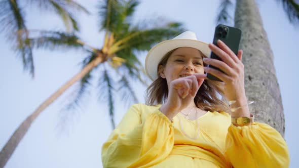 Beautiful Woman Using Smartphone on Tropical Island Under Green Palms at Summer