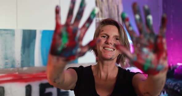 Cheerful caucasian senior woman shows colorful painted hands after art painting