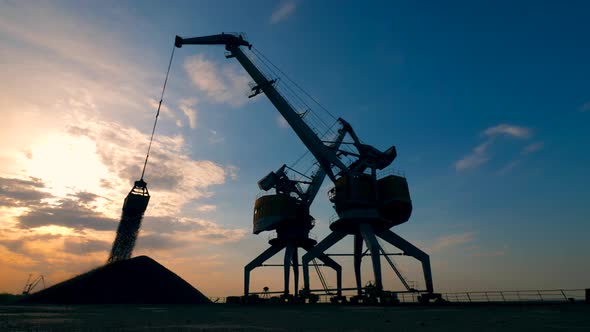 Dock Cranes Work with Rubble in a Sunset Background.