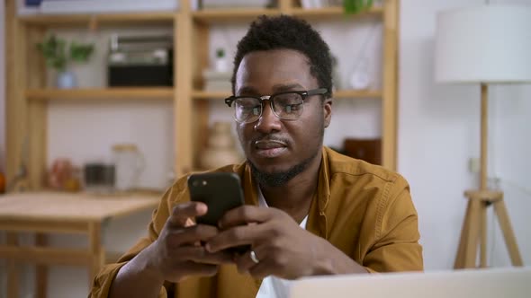 African Man on Smartphone Typing Message Background of Home Interior Spbas