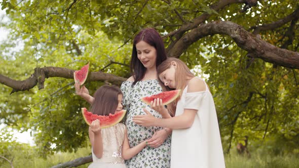 Pregnant Caucasian Woman and Her Two Pretty Daughters Standing Together in Hugs