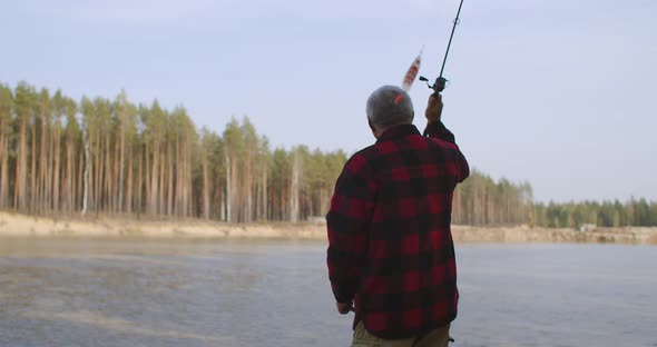 Fisherman Is Casting a Fishing Rod with Bait Inside Water of River, Standing on Shore, Fishing Trip