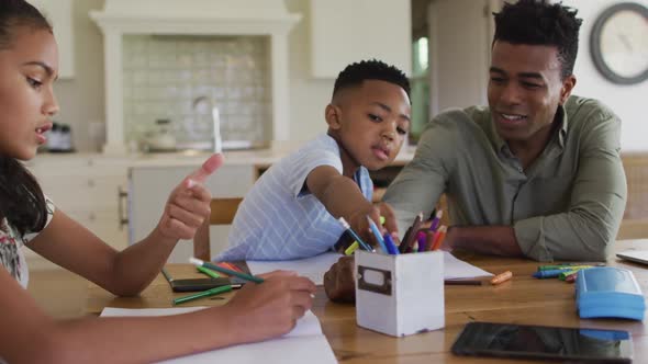 African american father, daugher and son sitting at kitchen table doing homework