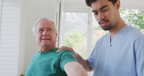 Male physiotherapist rotating retired senior man's hand in clockwise motion at retirement home
