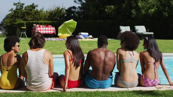 Diverse group of friends sitting in a row looking at the camera at a pool party