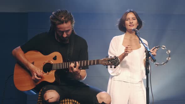 Female Singer with Tambourine and Musician Playing Guitar Performing on Stage