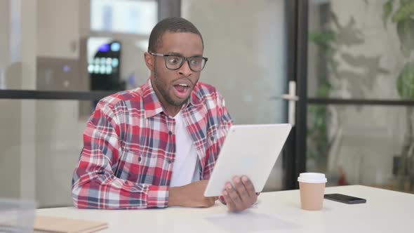 African Man Celebrating Success on Tablet in Office