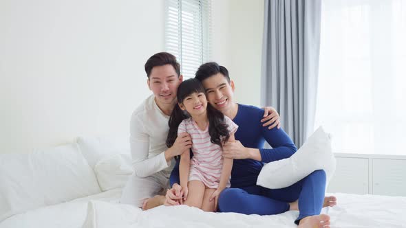 Portrait of handsome man gay family with young kid daughter sit on bed in morning in bedroom.