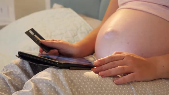 Closeup of Pregnant Woman with Big Belly Holding Credit Card and Using Tablet Computer for Doing