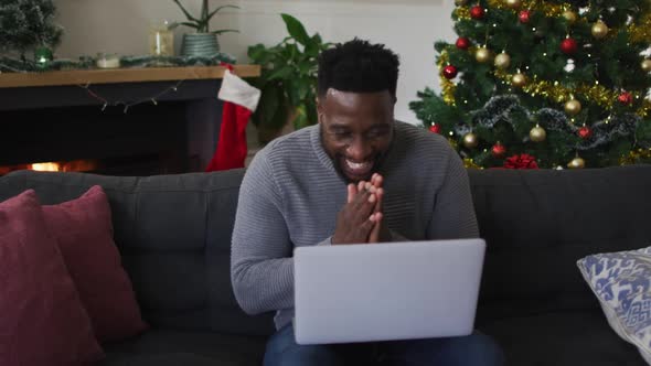 Smiling african american man having video call, sending kisses, christmas decorations in background