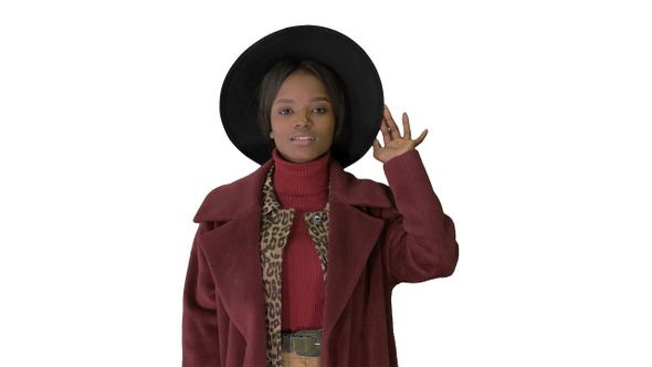 Cute afro model in coat touching hat walking on white background.