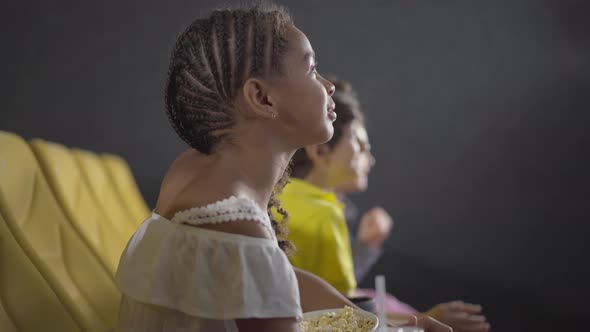 Side View of African American Girl Watching Film in Cinema. Happy Smiling Child Sitting in Movie