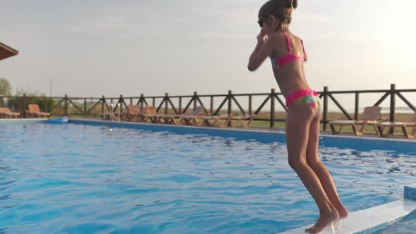 A Girl with Swimming Goggles Jumps Into a Pool with Clear Water on the Background of a Warm Summer