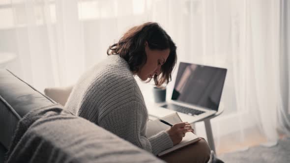 A Young Woman Making Notes in Her Notebook While Sitting on the Couch