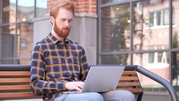 Redhead Beard Young Man working on Laptop, Sitting Outdoor on Bench