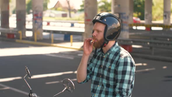 Portrait of Man Motorcyclist Smokes a Cigarette While Sitting on a Motorcycle at Street