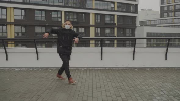 Young Guy in a Protective Mask During a Coronavirus Walks on the Roof and Dances