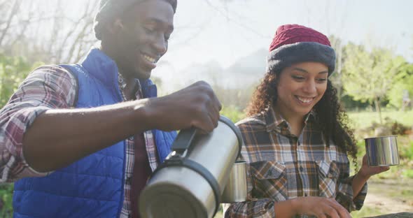 Smiling diverse couple drinking tea and hiking in countryside