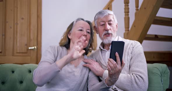 an Elderly Couple Sitting in Their Cozy House Communicates Via Video Call with Their Relatives While