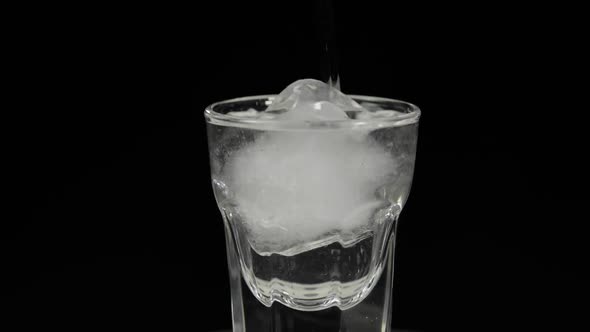 Pour Vodka Into Shot Glasses with Ice Cubes Placed on a Black Background