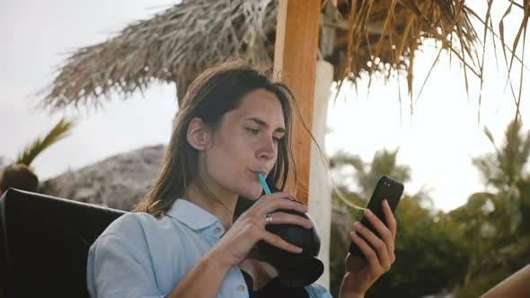 Happy Relaxed Tourist Woman Watching Online Video on Smartphone Smiling, Resting in Beach Chair on