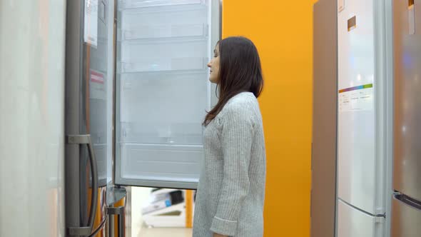 Young Woman in a Home Appliance Shop Chooses a Refrigerator